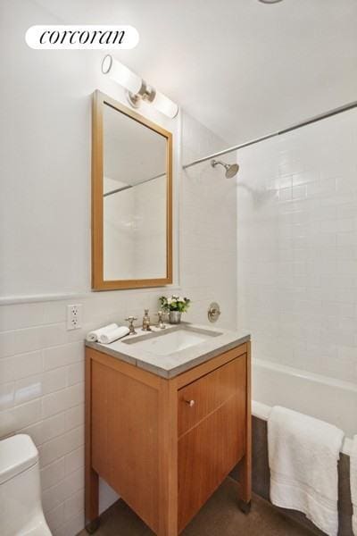 full bathroom with tiled shower / bath, vanity, toilet, and tile walls