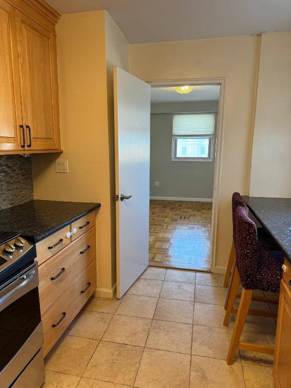 kitchen featuring light brown cabinetry, tasteful backsplash, dark stone countertops, light tile patterned floors, and stainless steel range