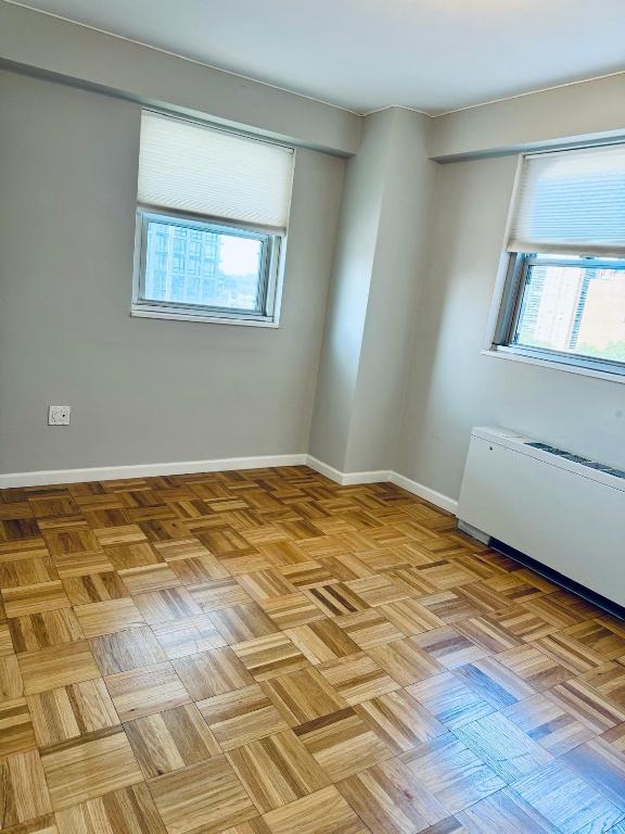 unfurnished room featuring radiator heating unit, a wealth of natural light, and light parquet floors