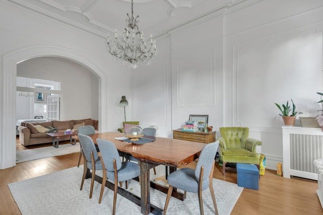 dining room with crown molding, a notable chandelier, radiator, and light wood-type flooring