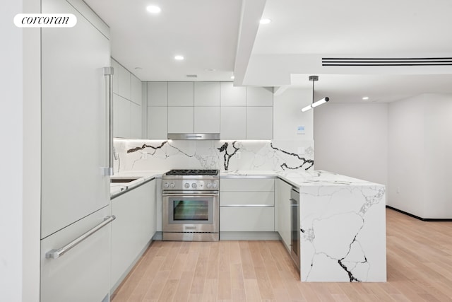 350 W 44th St Unit 101, New York City, NY 10036 - kitchen with premium appliances, modern cabinets, a peninsula, under cabinet range hood, and light stone countertops