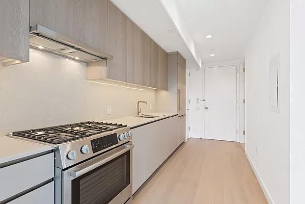 kitchen featuring sink, ventilation hood, light wood-type flooring, stainless steel range with gas cooktop, and gray cabinets