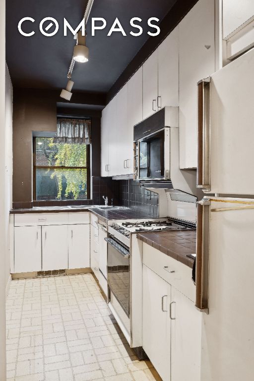 kitchen featuring white cabinetry, refrigerator, gas range gas stove, and backsplash