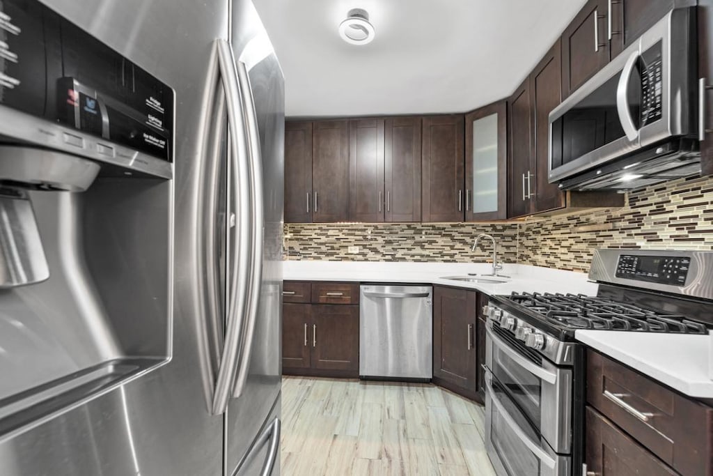 kitchen with stainless steel appliances, decorative backsplash, dark brown cabinetry, and sink