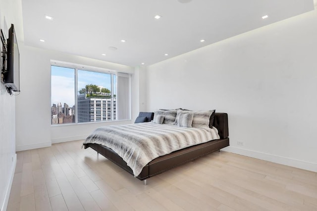 bedroom featuring light wood-type flooring, baseboards, a city view, and recessed lighting