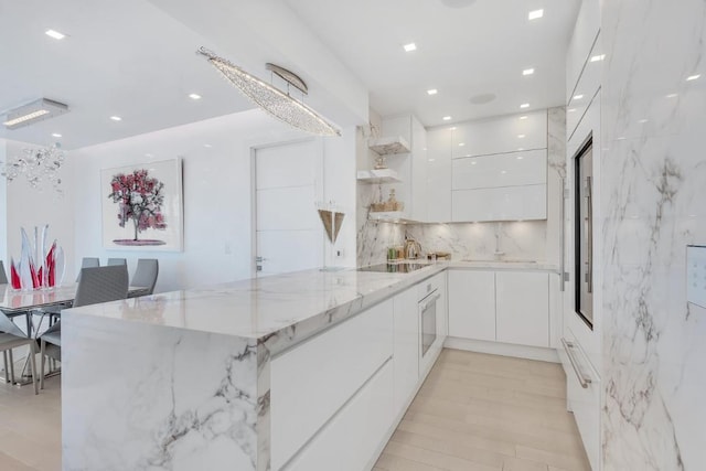 kitchen featuring light stone countertops, white cabinets, black electric cooktop, and kitchen peninsula