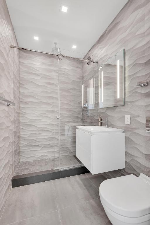 full bath featuring toilet, tile walls, a shower stall, and vanity