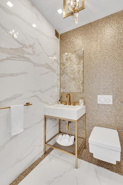 bathroom featuring a chandelier, marble finish floor, a sink, and tile walls