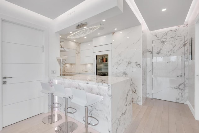 kitchen featuring light stone counters, a breakfast bar, white cabinetry, light wood finished floors, and modern cabinets