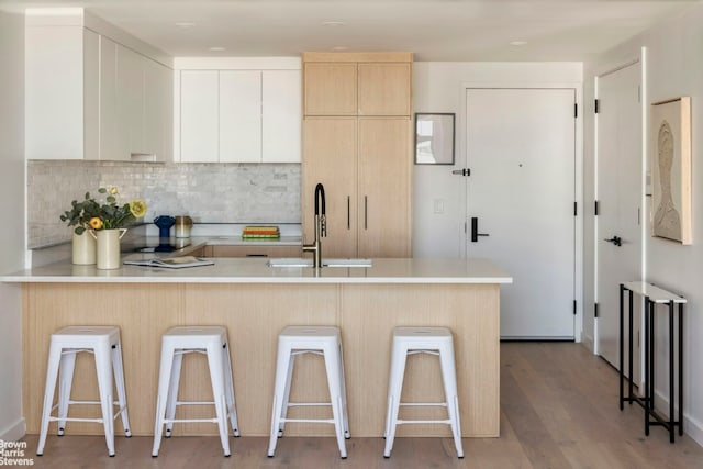 kitchen featuring kitchen peninsula, backsplash, a kitchen breakfast bar, light wood-type flooring, and sink