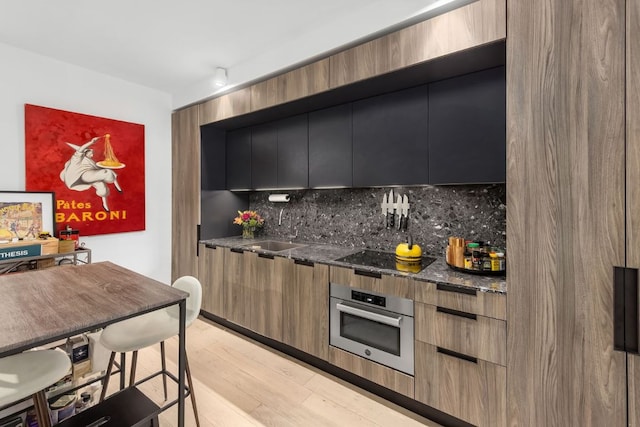 kitchen featuring sink, stainless steel oven, black electric cooktop, light hardwood / wood-style floors, and decorative backsplash