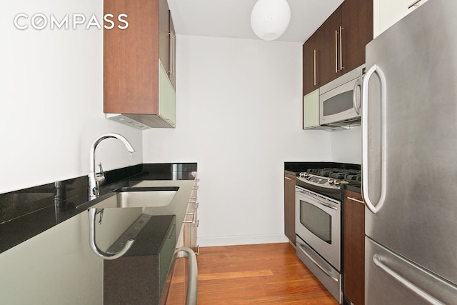 kitchen with dark countertops, light wood finished floors, appliances with stainless steel finishes, and a sink