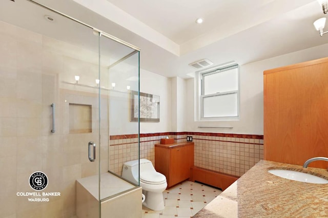 bathroom with tile walls, vanity, a shower with door, and toilet