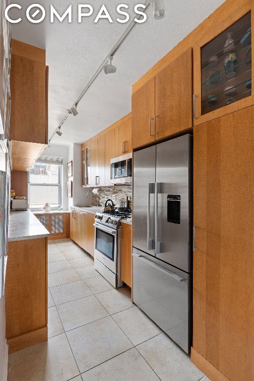 kitchen with light tile patterned floors, backsplash, track lighting, and stainless steel appliances