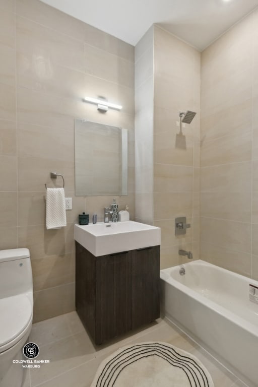 full bathroom featuring tiled shower / bath, tile walls, tile patterned flooring, vanity, and toilet