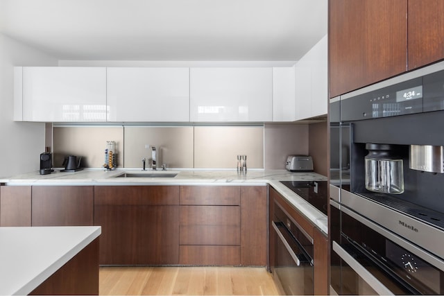 kitchen featuring brown cabinetry, a sink, light wood-style floors, black electric cooktop, and modern cabinets