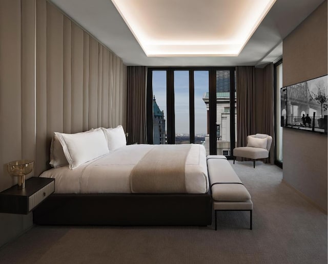 carpeted bedroom featuring a raised ceiling and expansive windows