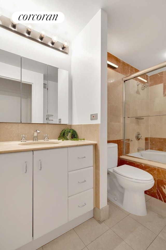 bathroom featuring tile patterned flooring, toilet, vanity, tile walls, and tiled shower / bath