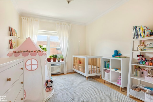 bedroom with a nursery area, an AC wall unit, ornamental molding, and light hardwood / wood-style floors