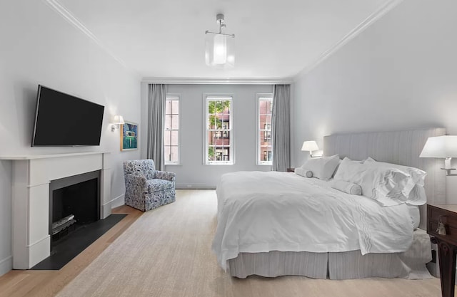 bedroom with wood finished floors, ornamental molding, and a fireplace with flush hearth