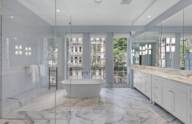 full bath with double vanity, marble finish floor, a freestanding tub, and a sink