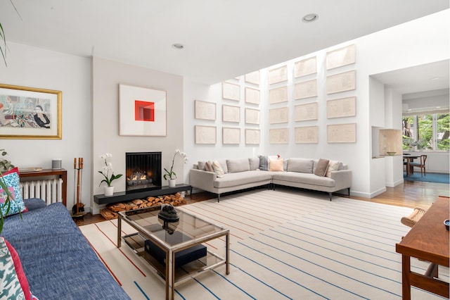 living area featuring a warm lit fireplace, baseboards, radiator heating unit, light wood-style flooring, and recessed lighting