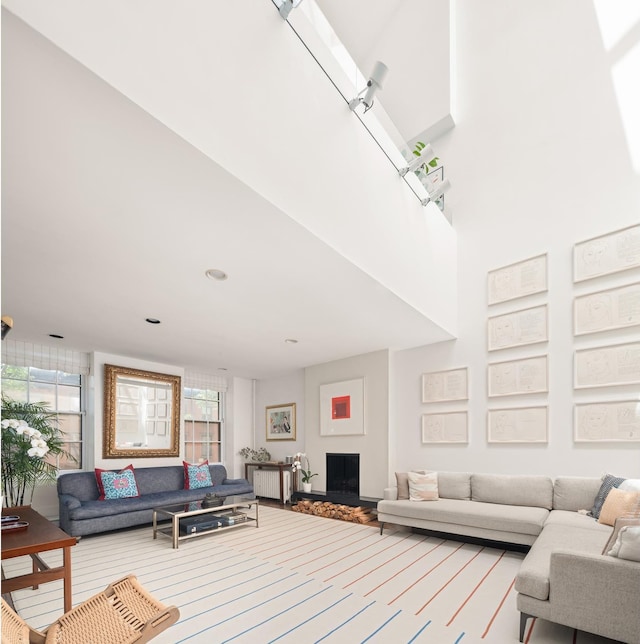 living area with radiator, a fireplace with raised hearth, and a towering ceiling