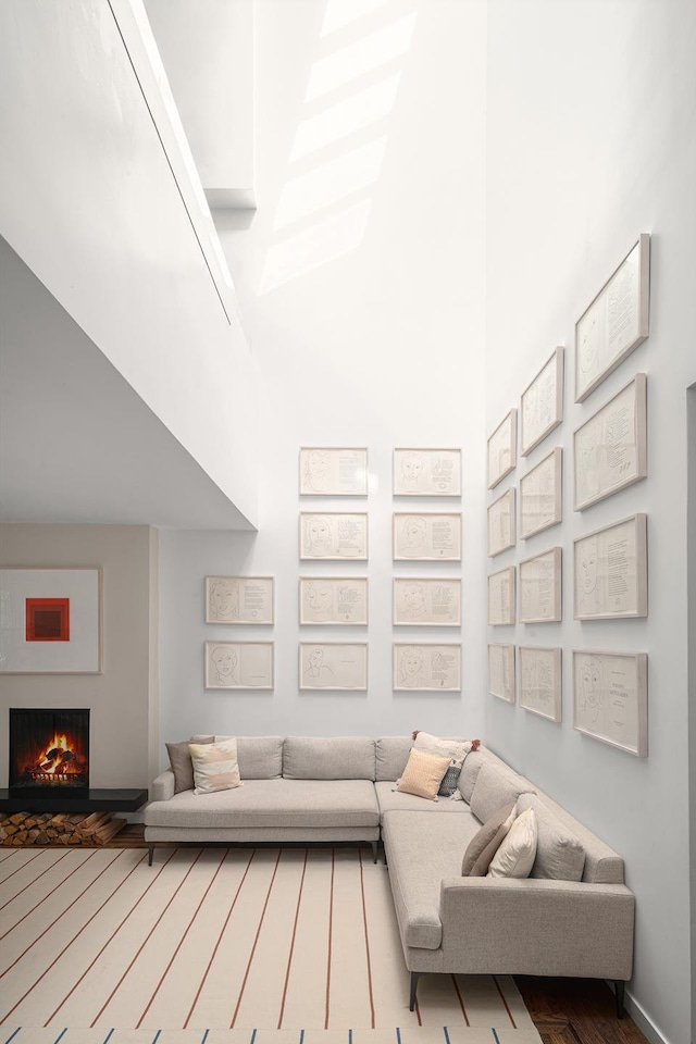 living area featuring a warm lit fireplace, wood finished floors, and a towering ceiling