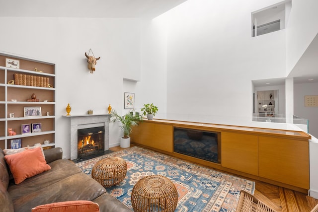 living area with a fireplace with flush hearth, a towering ceiling, and built in shelves