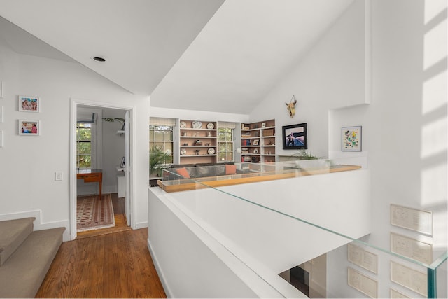 hallway featuring lofted ceiling, baseboards, wood finished floors, and stairway