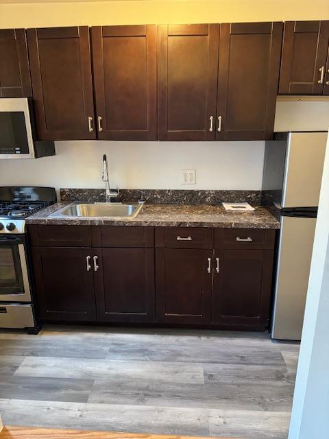 kitchen featuring stainless steel appliances, dark brown cabinets, sink, and light hardwood / wood-style flooring