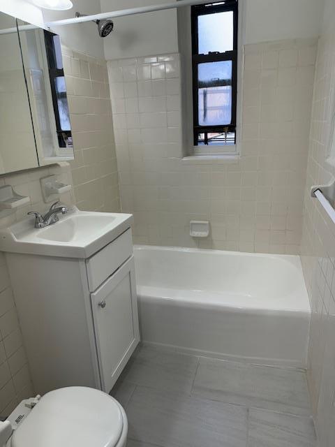 full bath with tile walls, toilet, vanity,  shower combination, and tile patterned floors