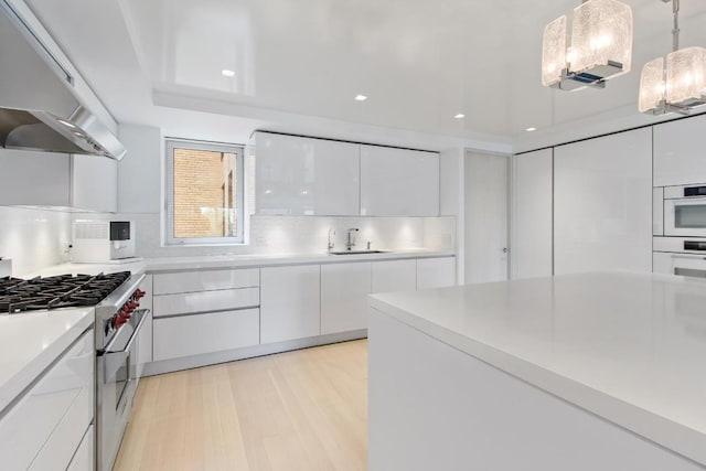 kitchen featuring pendant lighting, white cabinetry, sink, high end stainless steel range oven, and range hood