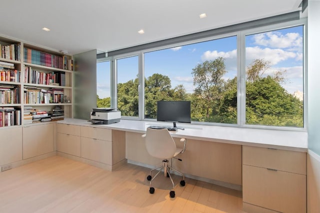 unfurnished office with built in desk, light wood-type flooring, and a wealth of natural light