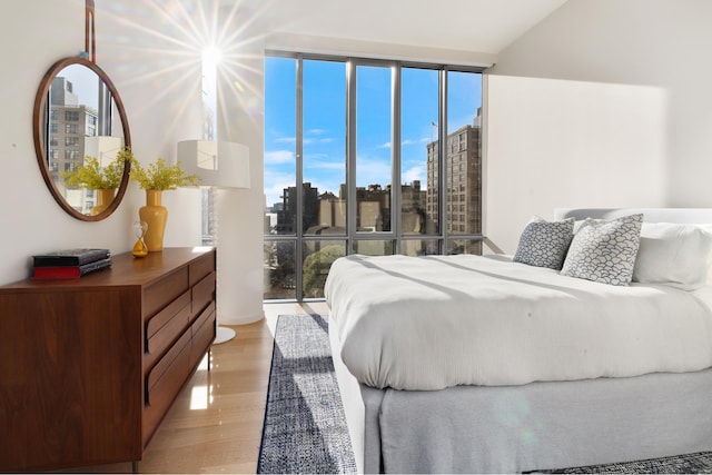 bedroom featuring a wall of windows, a view of city, and light wood-style flooring