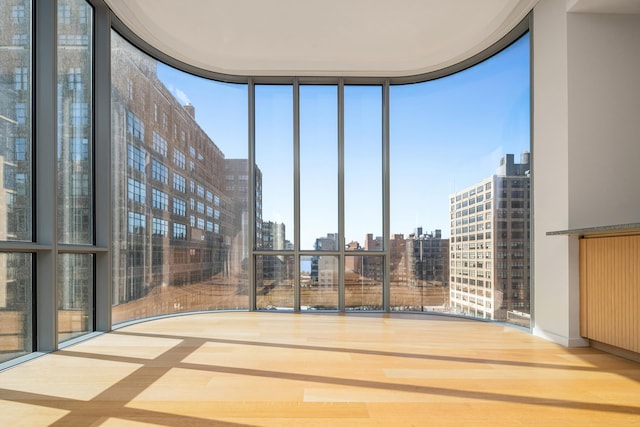 interior space with a wall of windows, wood finished floors, a view of city, and a healthy amount of sunlight