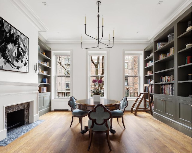 dining space featuring crown molding, built in features, a premium fireplace, an inviting chandelier, and light hardwood / wood-style floors