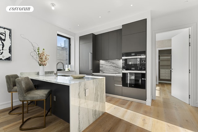 kitchen with multiple ovens, a kitchen bar, kitchen peninsula, backsplash, and light hardwood / wood-style flooring