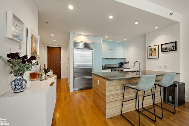 kitchen with light hardwood / wood-style floors, sink, built in fridge, a breakfast bar, and a center island