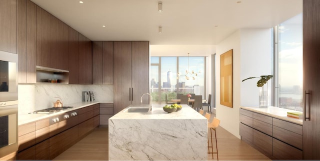 kitchen featuring tasteful backsplash, stainless steel gas stovetop, sink, wall oven, and a center island with sink