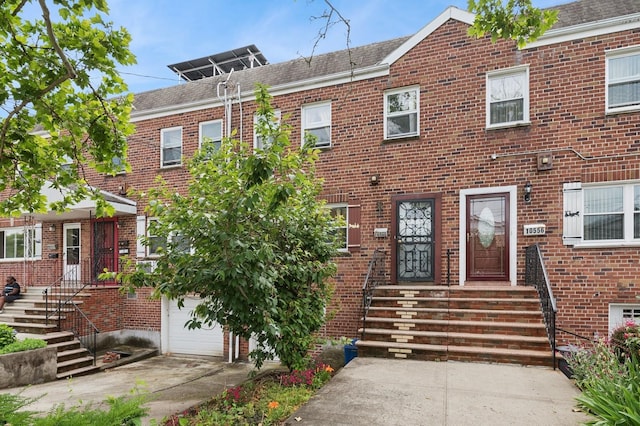 townhome / multi-family property with brick siding, driveway, a garage, and roof with shingles