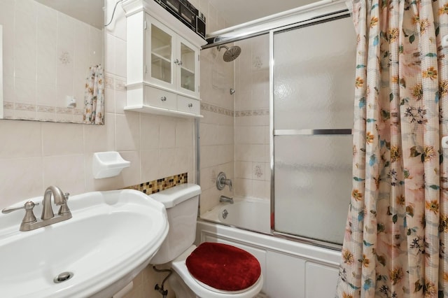 bathroom featuring toilet, a sink, backsplash, combined bath / shower with glass door, and tile walls