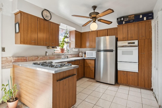 kitchen with light tile patterned floors, brown cabinets, white appliances, and a peninsula