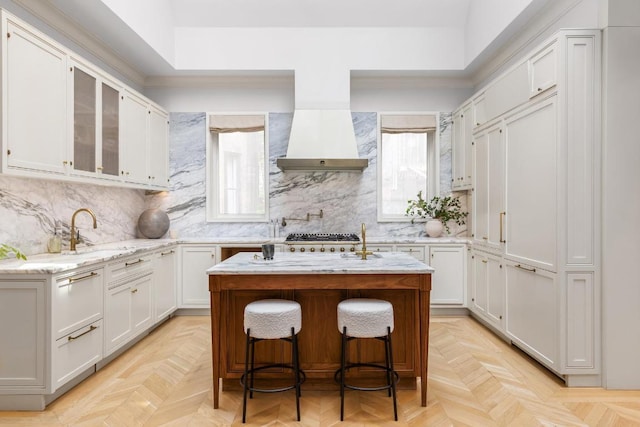 kitchen with premium range hood, white cabinetry, a kitchen breakfast bar, a kitchen island with sink, and light parquet floors