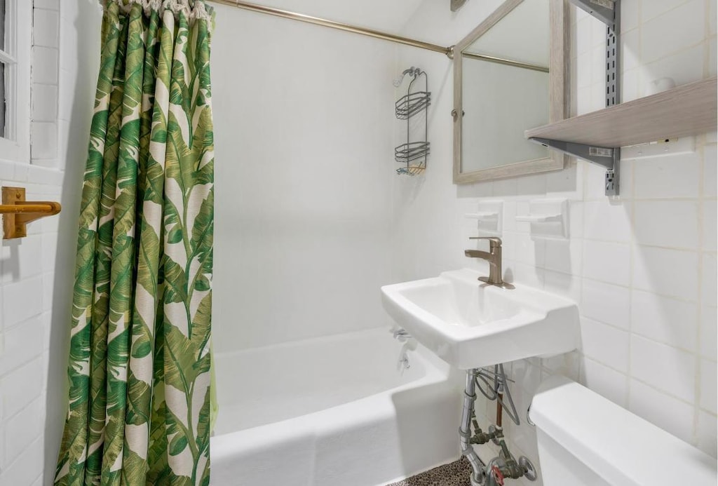 full bathroom featuring toilet, tasteful backsplash, shower / bath combination with curtain, tile walls, and sink