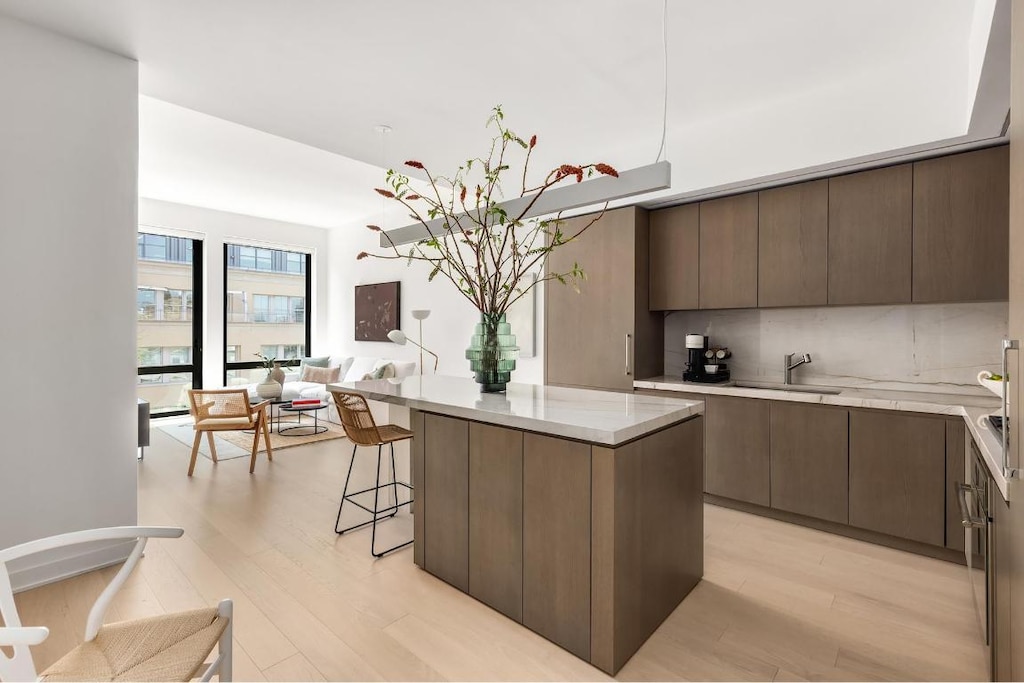 kitchen with dark brown cabinetry, a center island, sink, backsplash, and light wood-type flooring