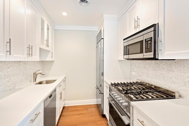 kitchen featuring sink, white cabinetry, light hardwood / wood-style flooring, ornamental molding, and appliances with stainless steel finishes