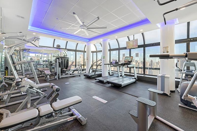 exercise room featuring a raised ceiling, floor to ceiling windows, a ceiling fan, and visible vents