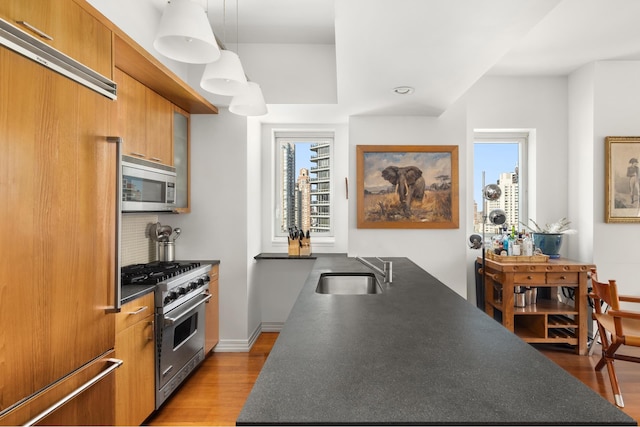 kitchen featuring brown cabinets, dark countertops, a sink, light wood-style floors, and premium appliances