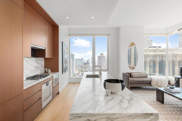 kitchen with wall oven, a city view, a sink, backsplash, and plenty of natural light